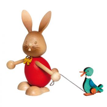 Wooden rabbit Stupsi with a red shirt pulls a small wooden duck behind him on a leash.