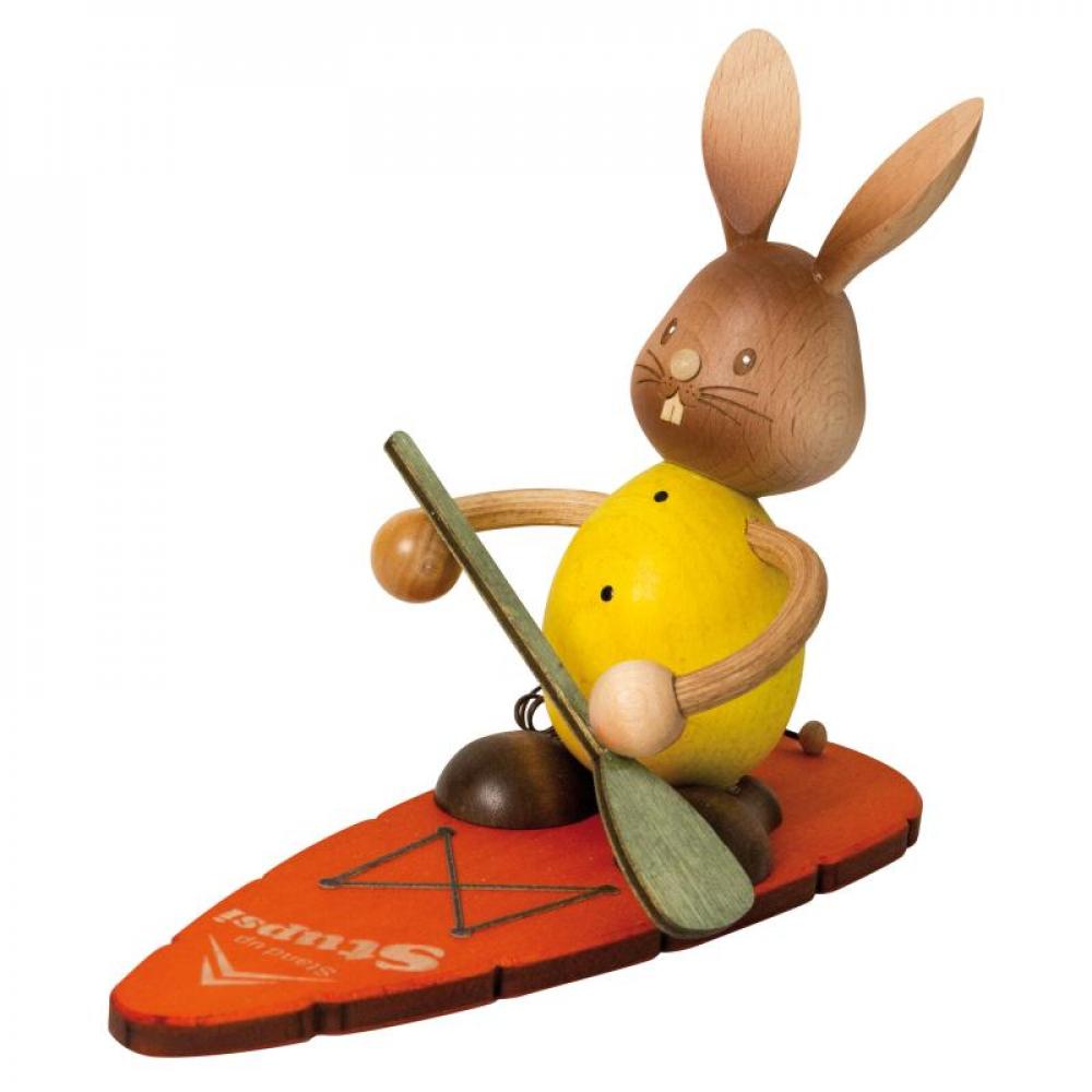 Wooden rabbit Stupsi with yellow shirt paddles standing on a board.