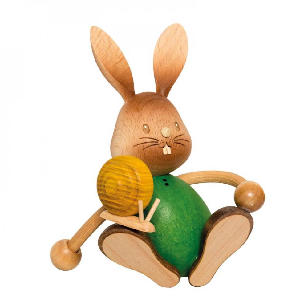 Wooden rabbit Stupsi with green shirt sits on the floor and a snail crawls over his leg.